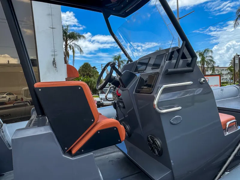Slide: The Image of 2023 Northstar Orion 7 boat cockpit with steering wheel and orange seating, under a blue sky. - 8