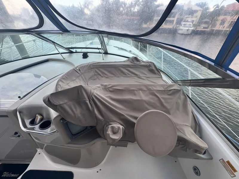 Slide: The Image of 1999 Sea Ray 400 Sundancer helm with covered controls, docked by waterfront homes. - 5