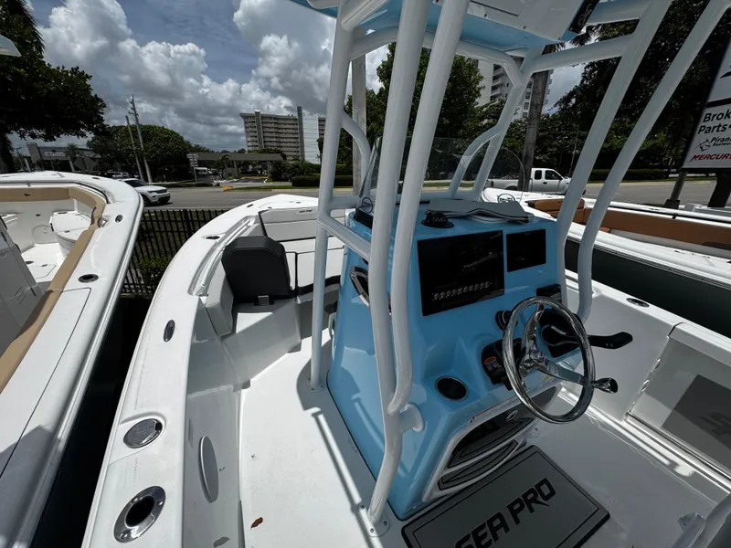 Slide: The Image of 2025 Sea Pro 225 Sandbar boat with blue console and steering wheel, docked outdoors. - 33