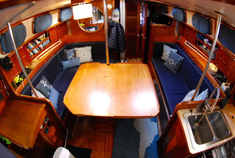 Slide: The Image of Interior of 1985 Endeavour 38 sailboat with wooden table, blue seating, and compact kitchen area. - 42