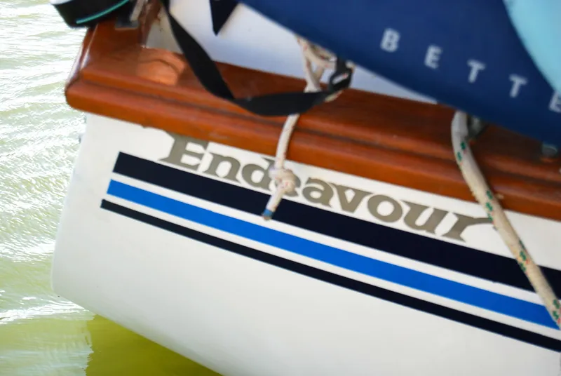 Slide: The Image of 1985 Endeavour 38 sailboat with blue stripes and wooden trim on water. - 7
