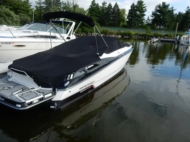 Slide: The Image of 2014 Monterey 288 Super Sport boat docked with black cover, calm water, and trees in background. - 11