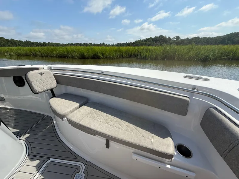 Slide: The Image of 2024 Sea Pro 262DLX boat interior with cushioned seating, near lush green marshland. - 22