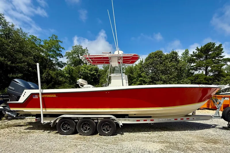 The Image of 2002 Contender 27 Tournament boat with red hull on trailer, parked outdoors. - 0