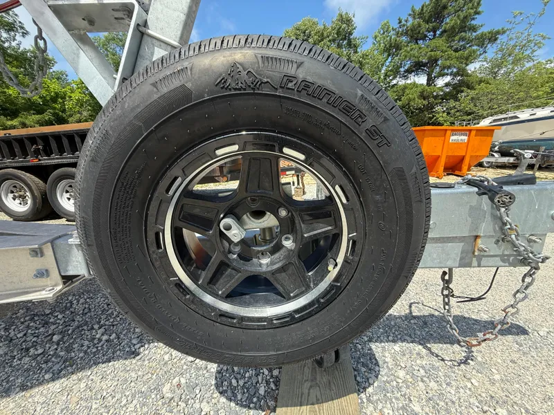 Slide: The Image of Trailer wheel on a Contender 27 Tournament boat trailer, 2002 model, parked on gravel. - 33
