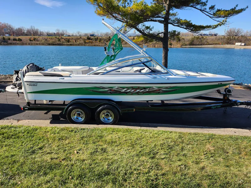 Slide: The Image of 2007 Tigé 22i boat on trailer by a lake, featuring green and white design. - 9