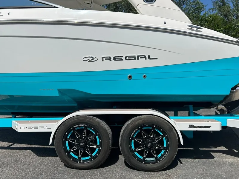Slide: The Image of 2022 Regal LS4 Surf boat on trailer with stylish black and blue wheels. - 14