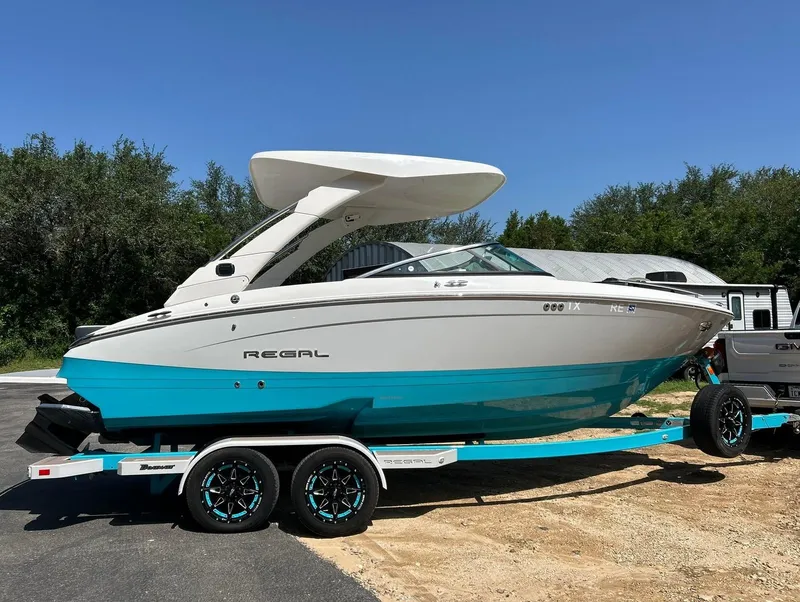 Slide: The Image of 2022 Regal LS4 Surf boat on trailer, parked outdoors under clear blue sky. - 18