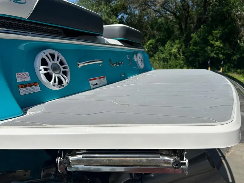 Slide: The Image of 2022 Regal LS4 Surf boat with speaker and swim platform, in a wooded setting. - 26