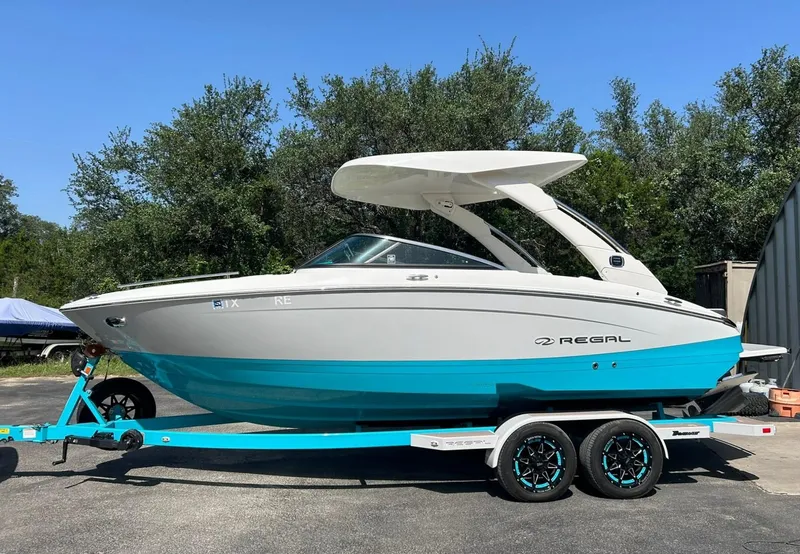 Slide: The Image of 2022 Regal LS4 Surf boat on trailer, white and blue design, parked outdoors. - 8