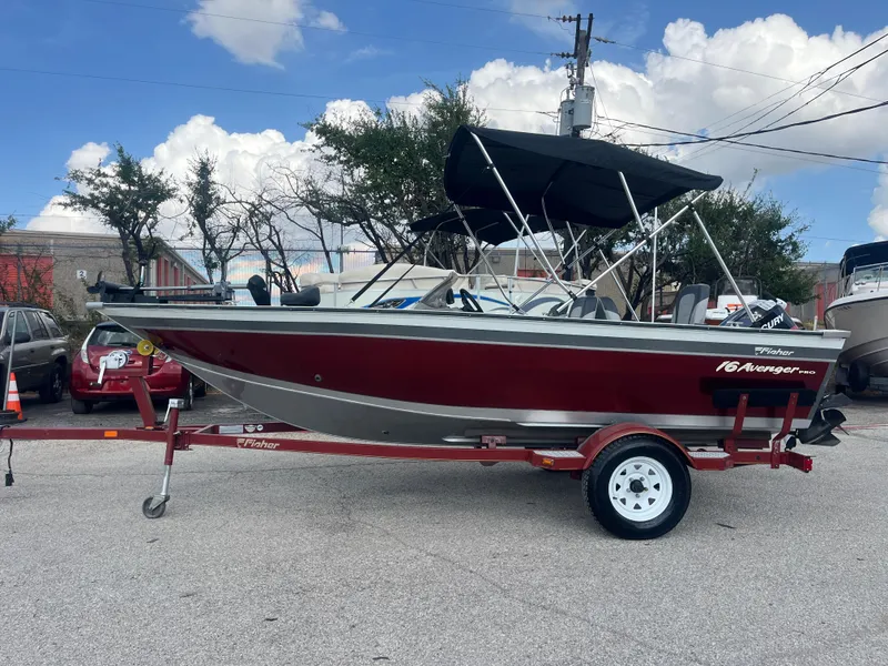 Slide: The Image of 2002 Fisher 16 Pro Avenger boat on trailer by a lake under a cloudy sky. - 1