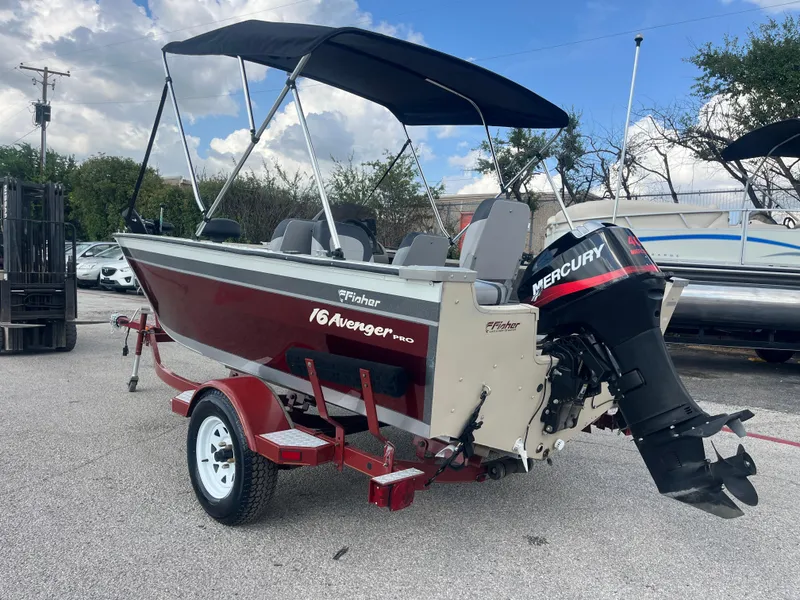 Slide: The Image of 2002 Fisher 16 Pro Avenger boat with canopy, parked on trailer near metal buildings. - 14
