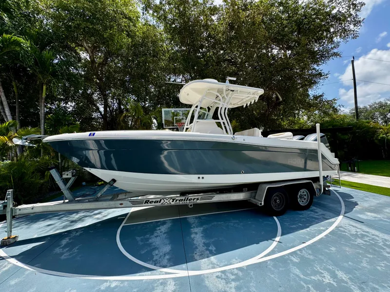 The Image of 2016 Robalo R260 Center Console boat on trailer, parked outdoors under trees. - 0