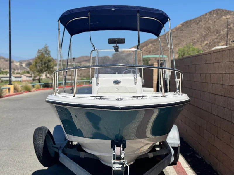 Slide: The Image of 2017 Edgewater 170CC boat on trailer with blue canopy, parked near brick wall. - 2