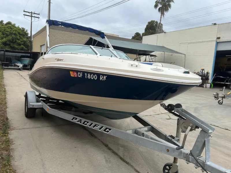 Slide: The Image of 2007 Sea Ray 185 Sport boat on trailer, parked outdoors near industrial buildings. - 2
