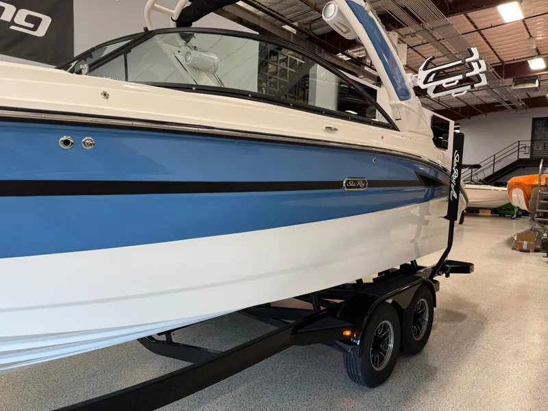 Slide: The Image of 2025 Sea Ray SDX250 Surf boat in showroom, blue and white exterior, on trailer. - 1