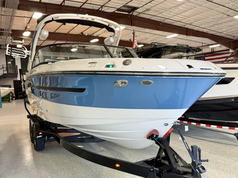 Slide: The Image of 2025 Sea Ray SDX250 Surf boat in showroom, blue and white exterior, on trailer. - 11