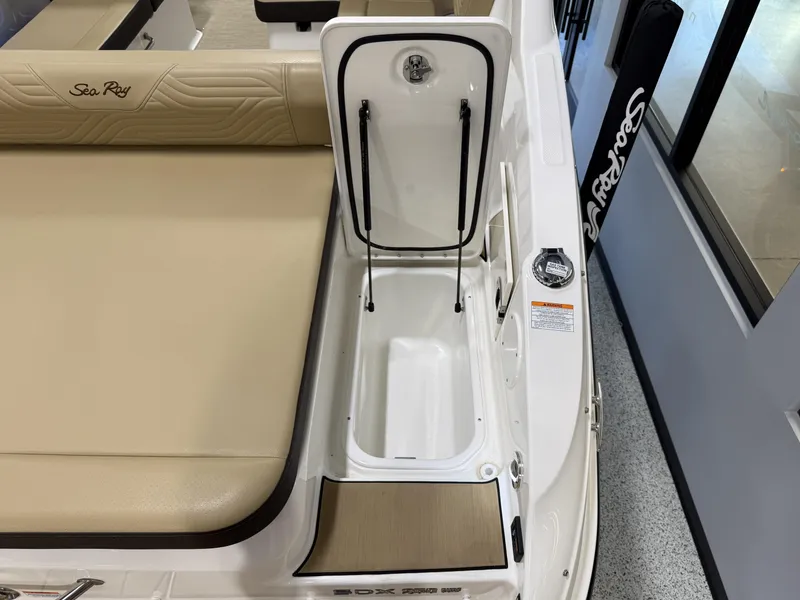 Slide: The Image of 2025 Sea Ray SDX250 Surf boat interior with open storage compartment and beige seating. - 40