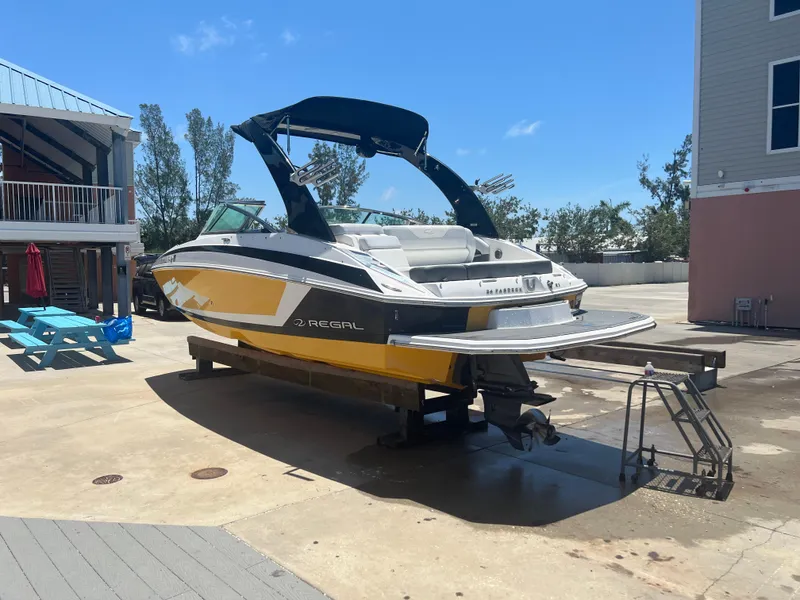 Slide: The Image of 2013 Regal 24 FasDeck RX boat on trailer, yellow and white, parked outdoors. - 2