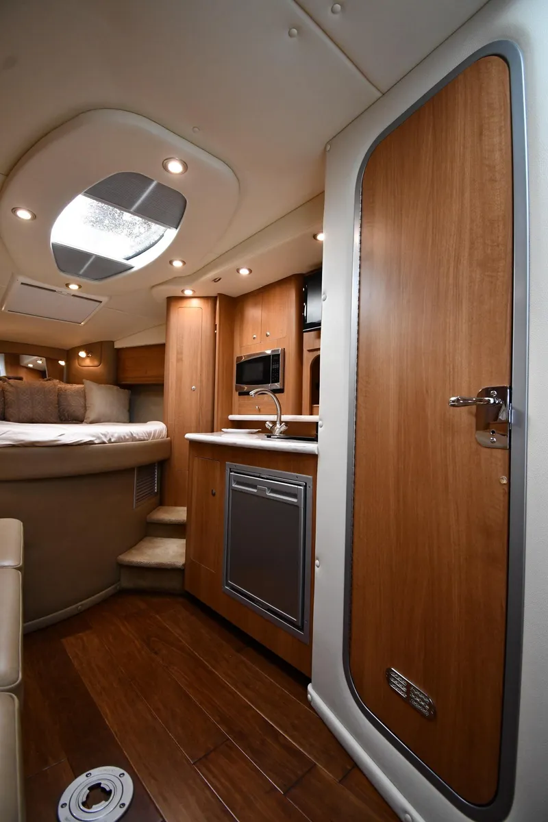 Slide: The Image of 2014 Rinker 310 Express Cruiser interior with wood finish, kitchenette, and cozy sleeping area. - 43