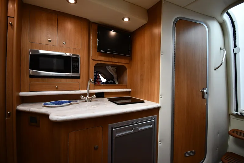 Slide: The Image of 2014 Rinker 310 Express Cruiser kitchen with microwave, sink, and wooden cabinetry. - 48