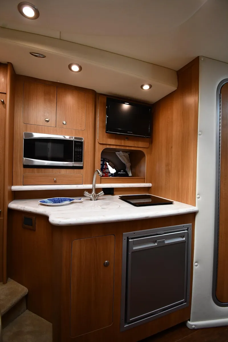 Slide: The Image of 2014 Rinker 310 Express Cruiser interior kitchen with microwave, sink, and TV. - 49