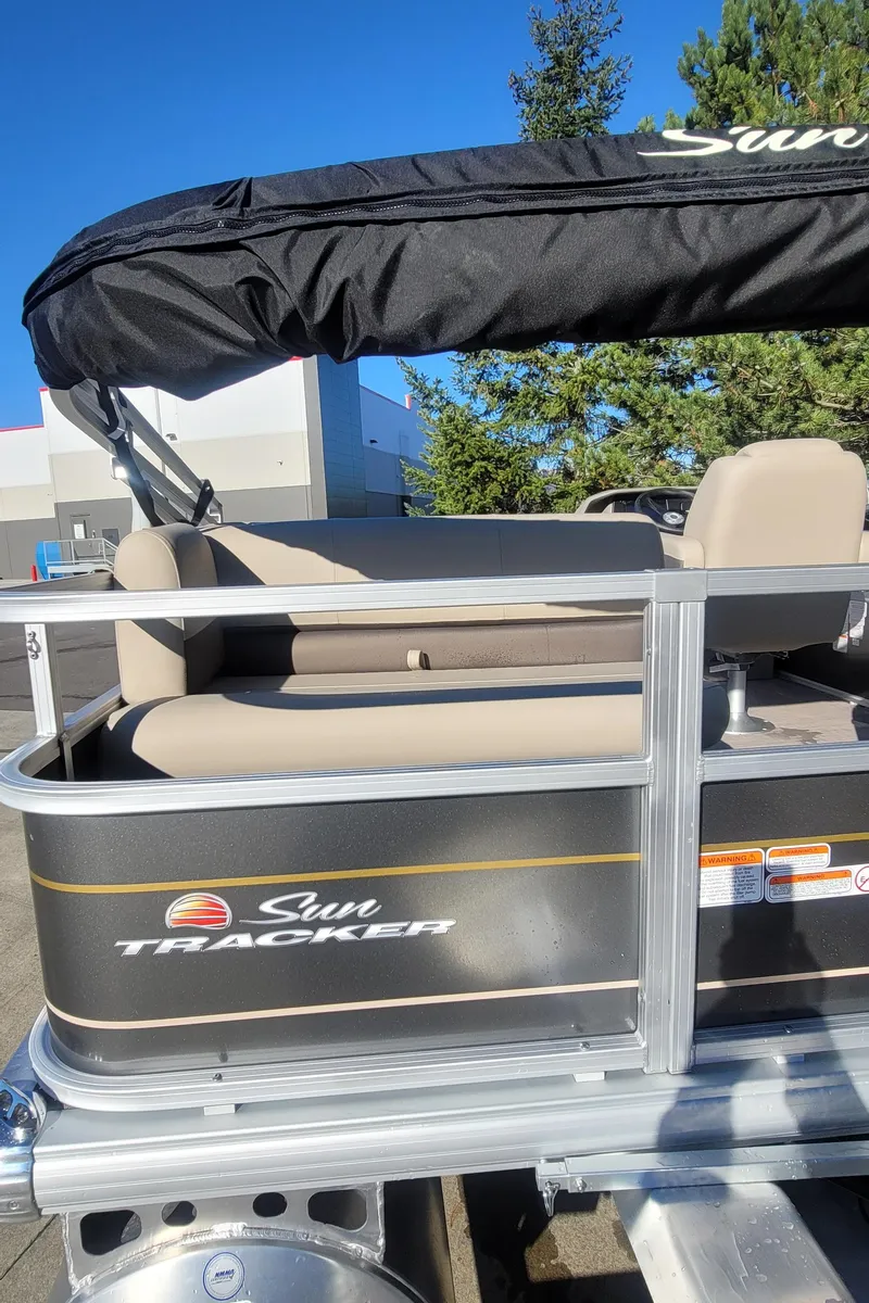 Slide: The Image of 2025 Sun Tracker Party Barge 18 DLX pontoon boat with canopy, parked outdoors. - 4