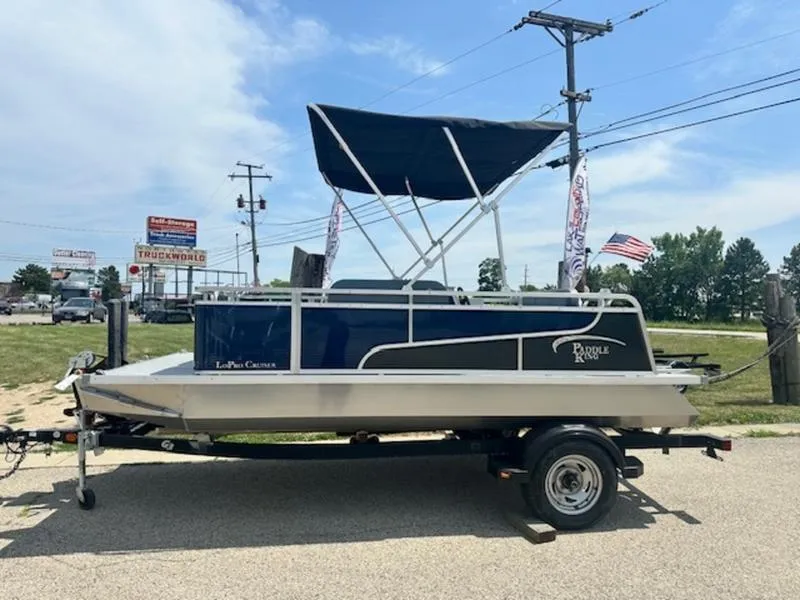 Slide: The Image of 2026 Paddle King Lo Pro Cruiser pontoon boat on trailer, parked outdoors. - 0