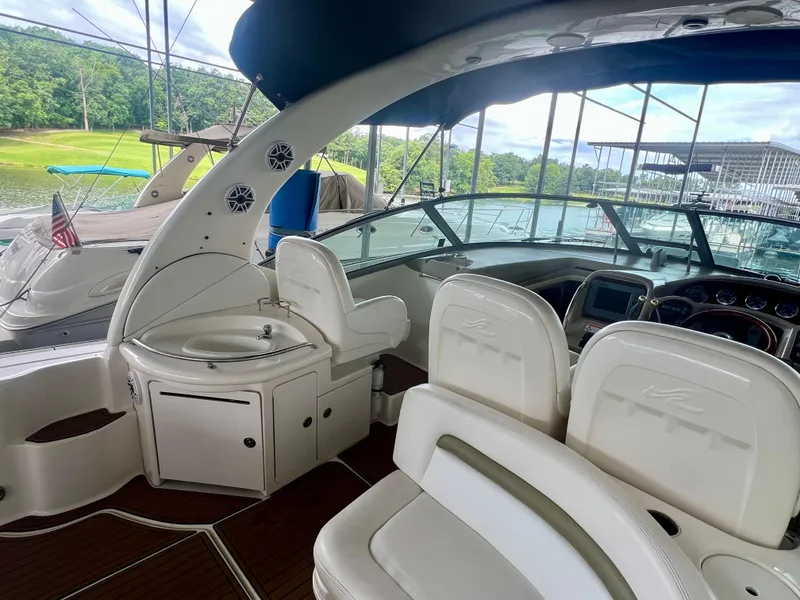 Slide: The Image of 2006 Sea Ray 340 Sundancer interior with helm, seating, and sink, docked by a scenic lake. - 8