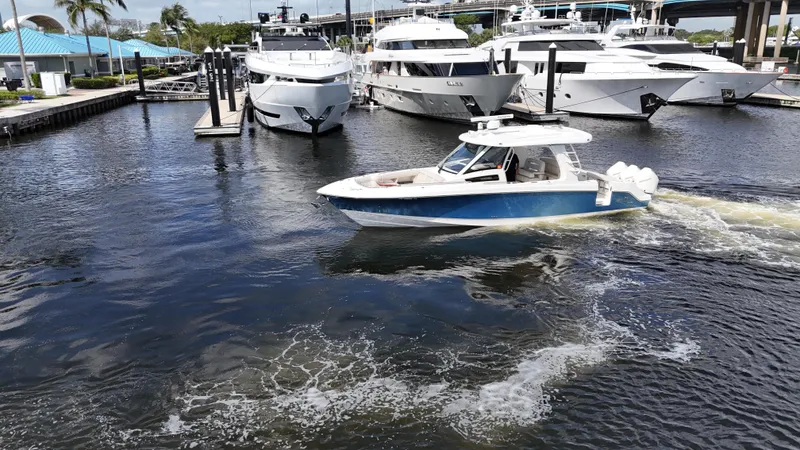 Slide: The Image of 2020 Boston Whaler 350 Realm cruising in marina with luxury yachts in background. - 12