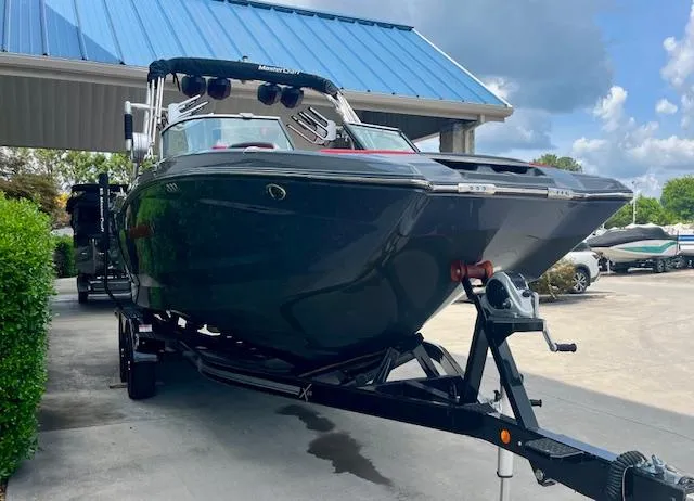 Slide: The Image of 2021 MasterCraft X24 boat on trailer under blue roof, parked outdoors. - 2