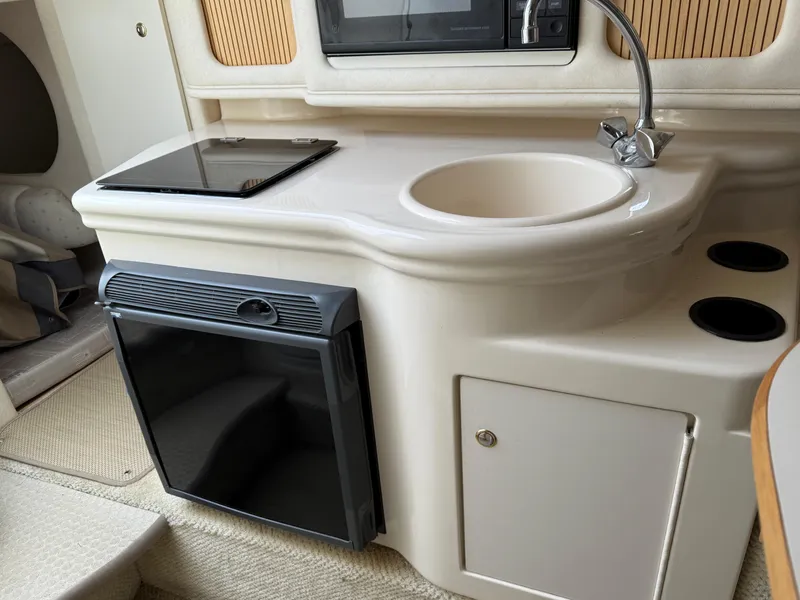 Slide: The Image of 2002 Sea Ray 260 Sundancer interior kitchenette with sink, stove, and mini fridge. - 10