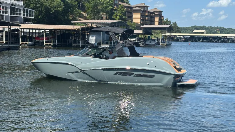 Slide: The Image of 2025 MB B52 25 Alpha boat cruising on a sunny lake near docks and buildings. - 9