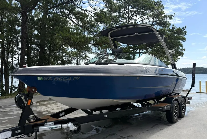 Slide: The Image of 2012 Malibu 21 Ride boat on trailer by lake, surrounded by trees. - 16