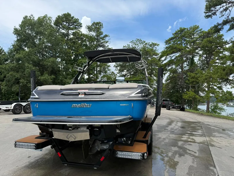 Slide: The Image of 2012 Malibu 21 Ride boat on trailer, surrounded by trees and a lake in the background. - 17