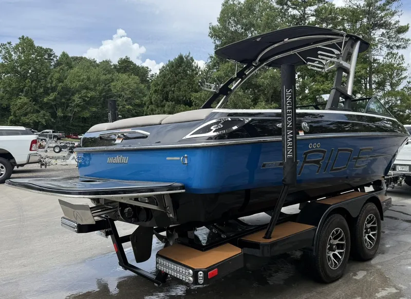 Slide: The Image of 2012 Malibu 21 Ride boat on trailer, blue and black design, parked outdoors. - 2