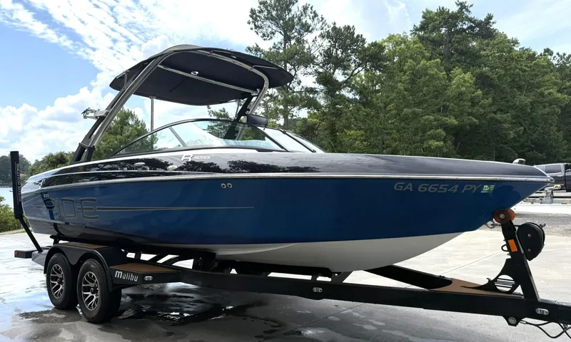 Slide: The Image of 2012 Malibu 21 Ride boat on trailer, blue and black, parked outdoors. - 4