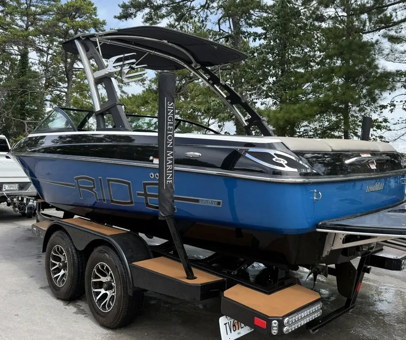 Slide: The Image of 2012 Malibu 21 Ride boat on trailer, blue and black, parked outdoors. - 5