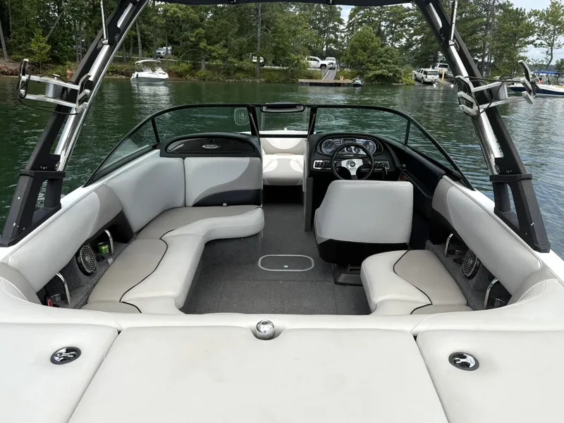 Slide: The Image of 2012 Malibu 21 Ride boat interior with seating and steering wheel, docked on a calm lake. - 6