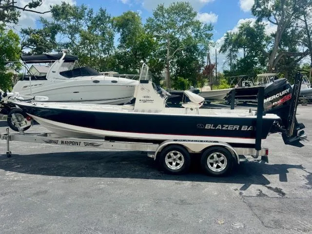 Slide: The Image of 2017 Blazer Bay 2170 boat on trailer, parked outdoors with trees and other boats in background. - 5