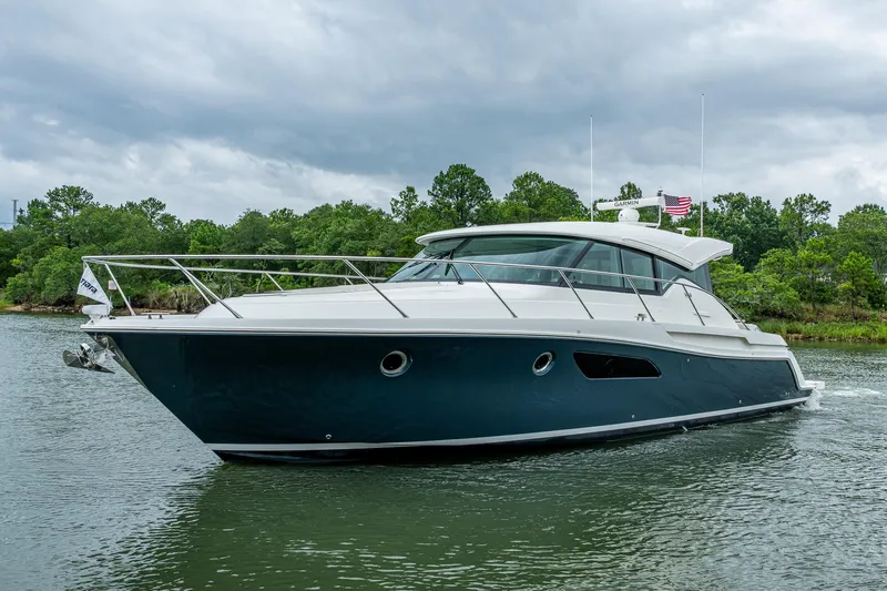 Slide: The Image of 2020 Tiara Yachts C44 Coupe cruising on a serene waterway with lush greenery. - 14