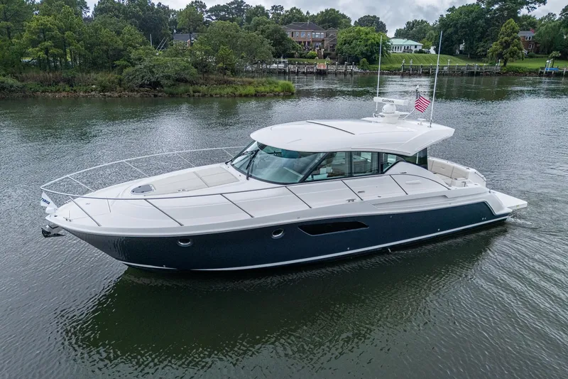 Slide: The Image of 2020 Tiara Yachts C44 Coupe cruising on a serene river with lush greenery. - 15