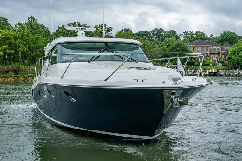 Slide: The Image of 2020 Tiara Yachts C44 Coupe cruising on a serene waterway with lush greenery. - 16