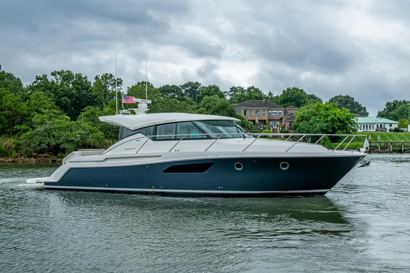 Slide: The Image of 2020 Tiara Yachts C44 Coupe cruising on a scenic waterway with lush greenery. - 18