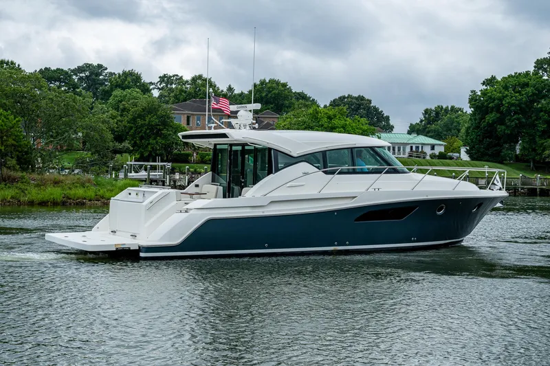 Slide: The Image of 2020 Tiara Yachts C44 Coupe cruising on a serene waterway, surrounded by lush greenery. - 20