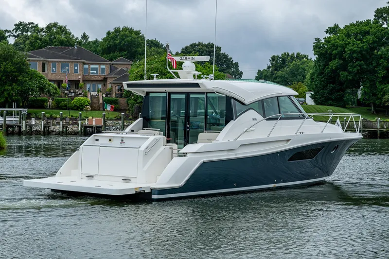 Slide: The Image of 2020 Tiara Yachts C44 Coupe cruising on a serene waterway near luxury homes. - 21