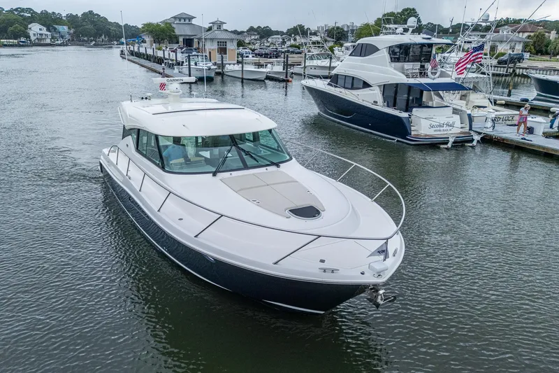 Slide: The Image of 2020 Tiara Yachts C44 Coupe cruising in a marina, surrounded by other boats. - 7
