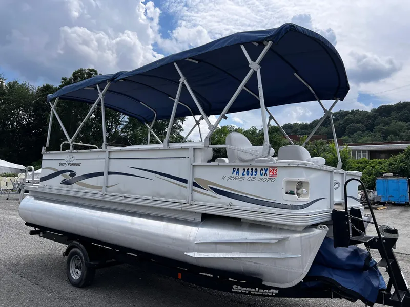 Slide: The Image of 2006 Crest II pontoon boat with blue canopy on a trailer, parked outdoors. - 2