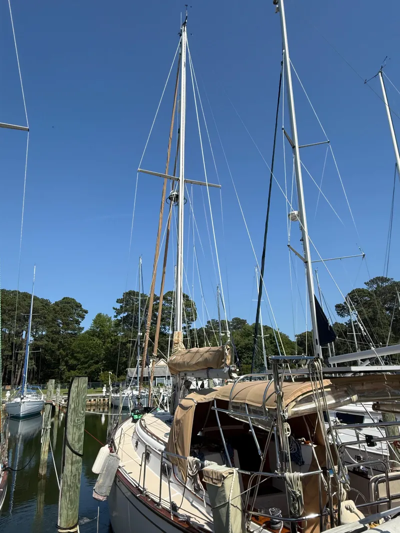 Slide: The Image of 1987 Island Packet 38 sailboat docked in a marina, surrounded by trees and clear blue sky. - 10