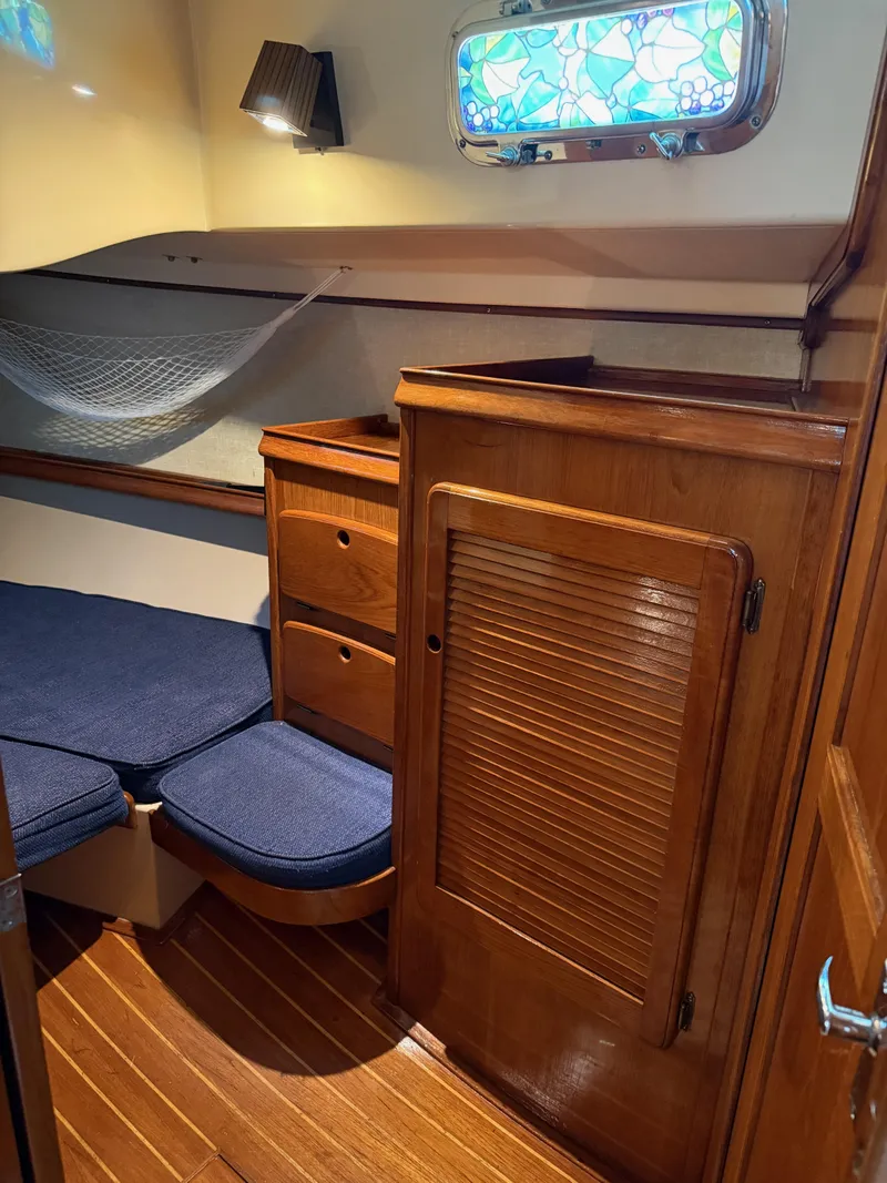 Slide: The Image of 1987 Island Packet 38 cabin interior with wooden cabinetry, blue cushions, and decorative window. - 20